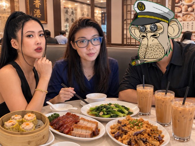 Two young women sit at a restaurant table with Chinese dishes including siu mai, roasted meats, vegetables, and milk tea, alongside a cartoon monkey captain avatar with a cigar.
