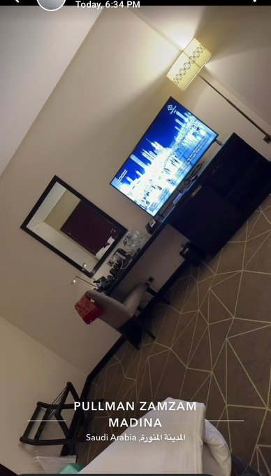 A vertically-oriented photo of a hotel room interior with a TV, mirror, and chairs, tagged with the location 'PULLMAN ZAMZAM MADINA, Saudi Arabia' taken at 6:34 PM.
