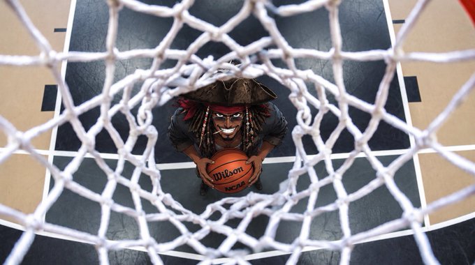 A person dressed as a pirate wearing a black hat and red bandana, viewed through a basketball net, holding a Wilson NCAA basketball.