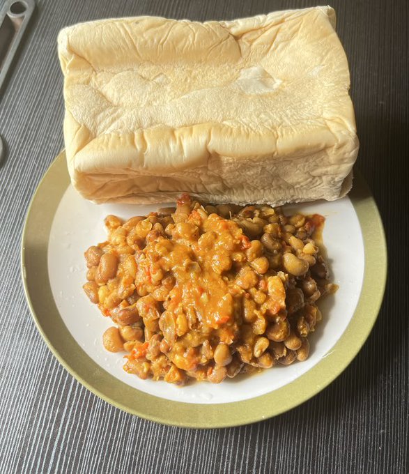 A plate with a large folded flatbread and a serving of baked beans in tomato sauce on a wooden surface.