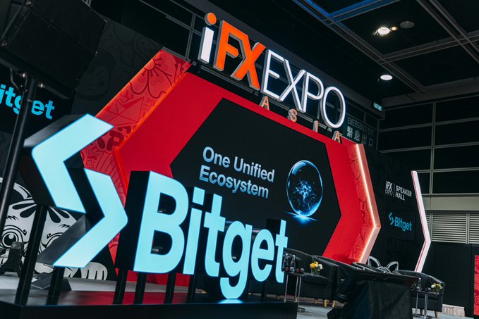 A photograph of the Bitget booth at the iFX EXPO ASIA, featuring large illuminated signage with the tagline 'One Unified Ecosystem' alongside the Bitget logo.