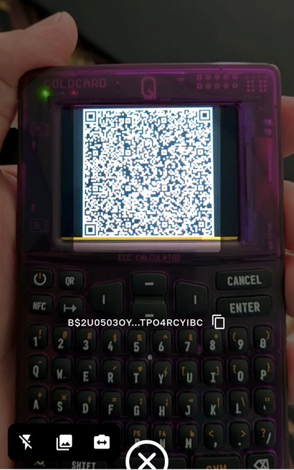 A close-up of a translucent purple Coldcard Q hardware wallet displaying a QR code on its screen, with a partial Bitcoin address visible below the device.