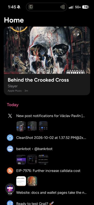 An iPhone home screen screenshot shows an Apple Music widget playing 'Behind the Crooked Cross' by Slayer, along with various notifications including posts from 'Václav Pavlín', 'CleanShot', 'bankrbot', and 'EIP-7976'.