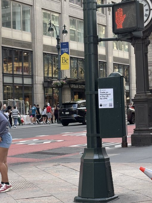 A poster on a street lamp reads "Trade on Hyperliquid in the US. No VPN." This likely relates to the accompanying post's mention of "Hyperliquid" by advertising a way to trade on the platform.
