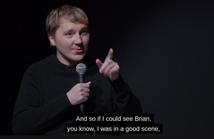 A man with short blonde hair speaking into a microphone against a black background, with a caption reading 'And so if I could see Brian, you know, I was in a good scene,'