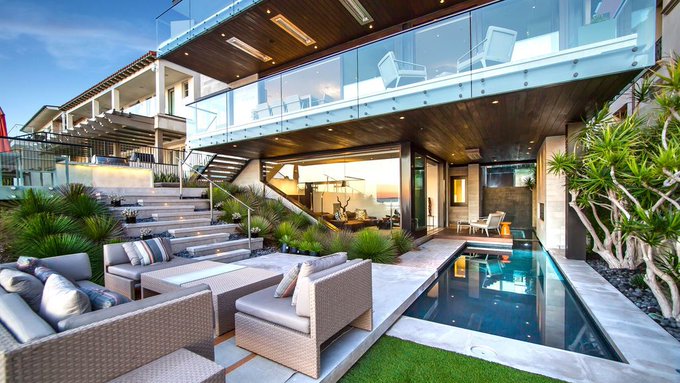 A modern, luxurious home features an outdoor patio with a swimming pool, lounge furniture, and a balcony with glass railings.