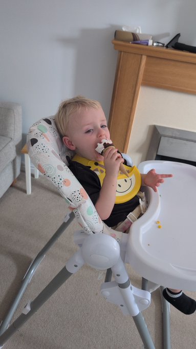 A toddler sits contentedly in a high chair, enjoying a chocolate treat while wearing a yellow smiley-face bib, with a "How it started... How it's ended" caption emphasizing his newfound love for the messy indulgence.