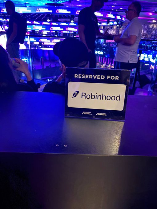 A sign at a gaming venue or casino reading 'RESERVED FOR Robinhood' with blue lighting illuminating the background where people are gathered.