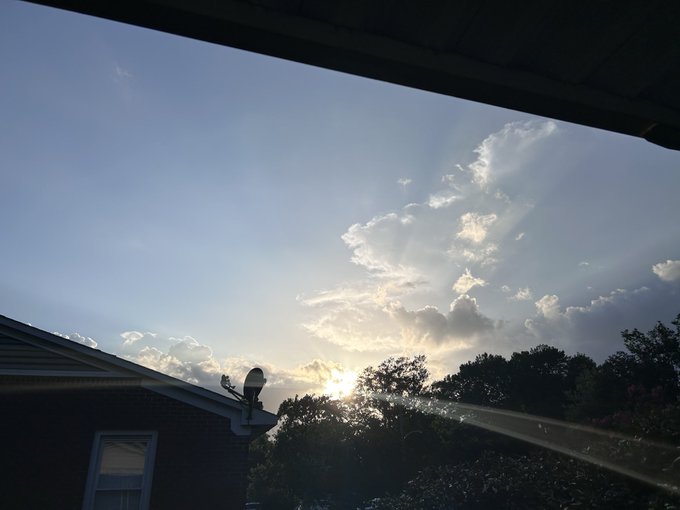 A stunning sunset sky filled with dramatic sunbeams breaking through scattered clouds, viewed from beneath a rooftop overhang with trees and a satellite dish in silhouette. The peaceful, golden-hour atmosphere perfectly matches the relaxed "Vibes & Views" mood of the post.
