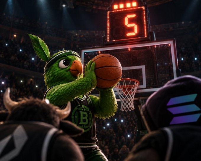 A green bird mascot in a Boston Celtics jersey holding a basketball near a hoop with a shot clock showing '5' in a crowded arena.