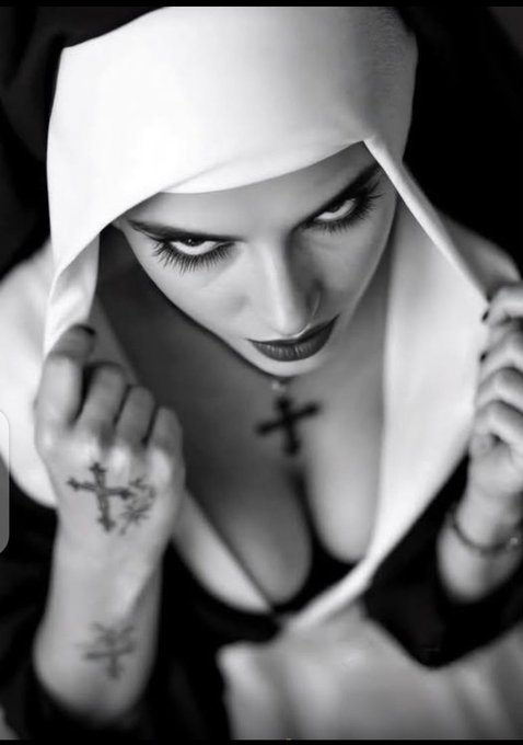 A dramatic black-and-white portrait of a woman wearing a nun's habit, looking downward with intense dark eye makeup and dark lipstick, with a small cross pendant at her chest and an ornate cross tattoo visible on the back of her hand.