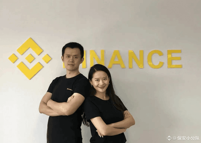 Two people in black shirts stand back-to-back with crossed arms in front of a yellow 'BINANCE' logo.