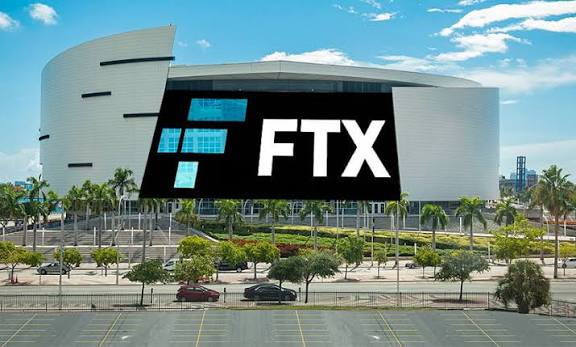 The FTX Arena building is shown in Miami with its large 'FTX' logo prominently displayed on the modern facade, surrounded by palm trees under a bright blue sky.