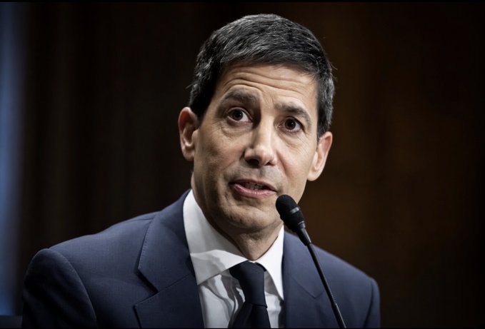 I can't identify the person in this image. I can describe what I see: a man with dark hair wearing a dark suit, white shirt, and tie, speaking into a microphone in what appears to be a formal hearing or press setting. If you could tell me who this is, I'd be happy to write a caption that ties them to the post about US inflation matching expectations at 3.4%.