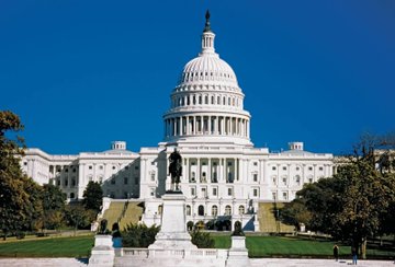 A clear, sunny day view of the United States Capitol building in Washington D.C., featuring its iconic white dome and surrounding grounds.
