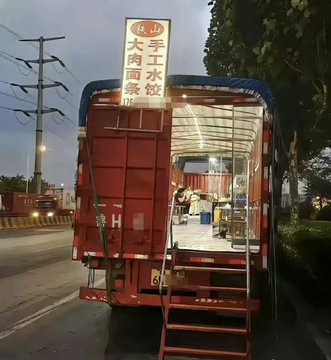 A red truck with Chinese characters reading '泉出手工水饺' (Quan Chu Handmade Dumplings) parked on a street at dusk, with its rear doors open revealing a food preparation area inside.