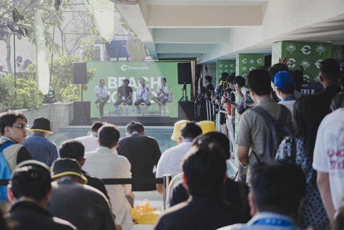 At Coinfest Asia 2026, a Tokocrypto panel discussion titled "BEACH C..." takes place on a green-themed stage where speakers address an audience of attendees, reinforcing the post's emphasis on crypto education, risk awareness, and long-term strategy as accessibility grows.