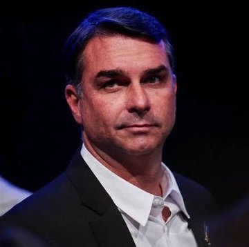 A man with dark hair wearing a black suit jacket and white shirt looks thoughtfully off-camera at what appears to be a political event. The image relates to the post as it likely depicts Flávio Bolsonaro, whose rising approval rating on Polymarket is highlighted alongside Lula's declining political standing.