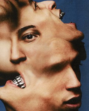 An artistic close-up photograph showing two faces pressed together with hands gripping the heads, featuring metallic rings on the fingers.