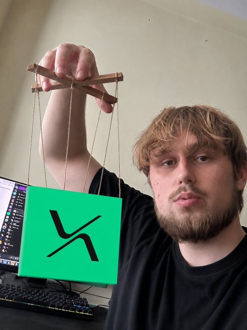 A man holds up a green sign with the black 'X' logo of the social media platform X, controlled by strings like a marionette.