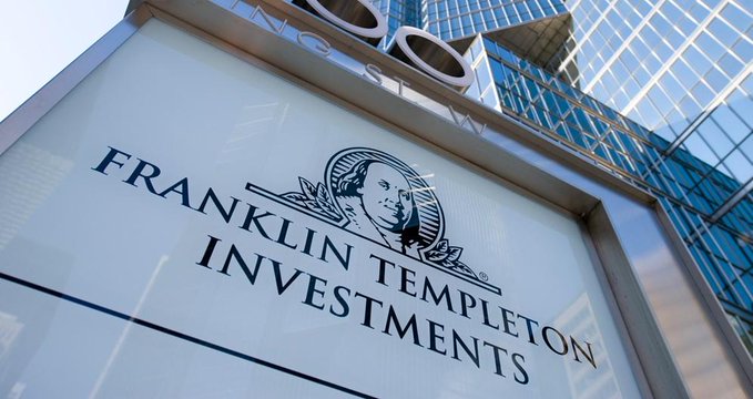 A close-up of a 'FRANKLIN TEMPLETON INVESTMENTS' sign featuring Benjamin Franklin's portrait, mounted in front of a glass building.