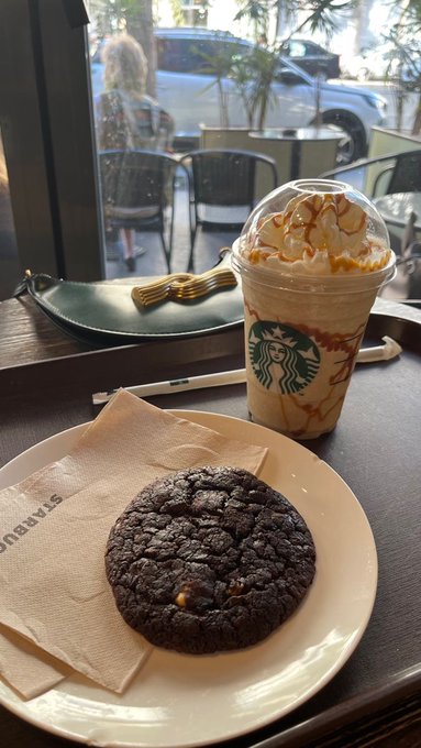 A Starbucks caramel Frappuccino sits beside a large chocolate cookie on a café table, with the recognizable Starbucks logo visible on the cup—evoking a small everyday indulgence that, like a speculative crypto buy, tempts the wallet but warrants a quick gut check before the purchase.