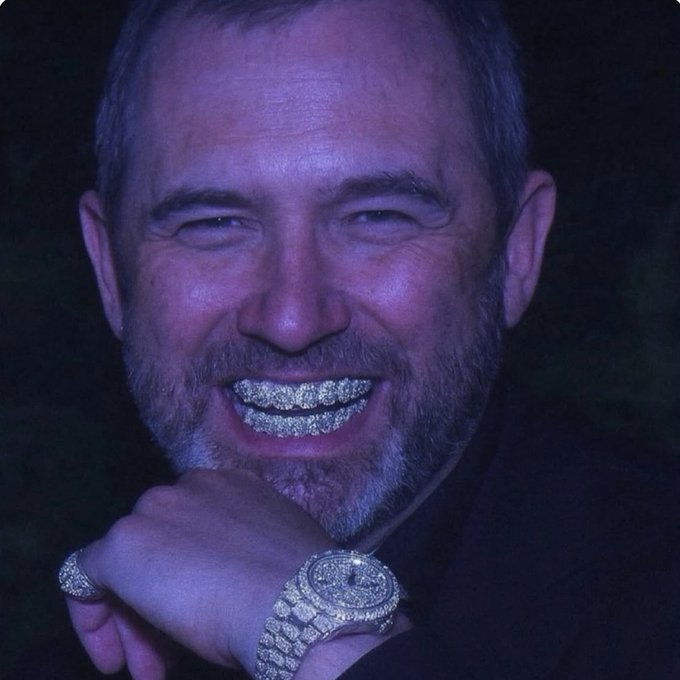 A close-up photo of a smiling man wearing elaborate diamond-encrusted grillz on his teeth, along with a diamond ring and a diamond-encrusted watch.
