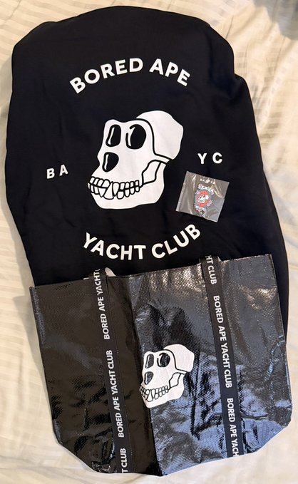 A black Bored Ape Yacht Club (BAYC) t-shirt featuring the signature skull logo, displayed alongside matching branded packaging.