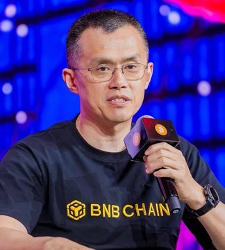A man wearing a black t-shirt with the "BNB CHAIN" logo speaks into a microphone during what appears to be a conference or interview. The image relates to the post by featuring CZ (Changpeng Zhao), founder of Binance and a key figure in the BNB Chain ecosystem, discussing Bitcoin's role as a hedge against inflation.
