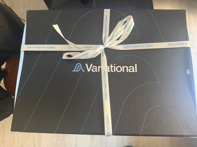The image features a black box with a white ribbon tied around its neck, sitting on top of a table or countertop. The ribbon has the words "VARIANTIAL" written on it. The background appears to be a plain white wall, which contrasts nicely with the dark color of the box and ribbon. There is no text visible in the image, but the focus seems to be on the black box and its ribbon design.