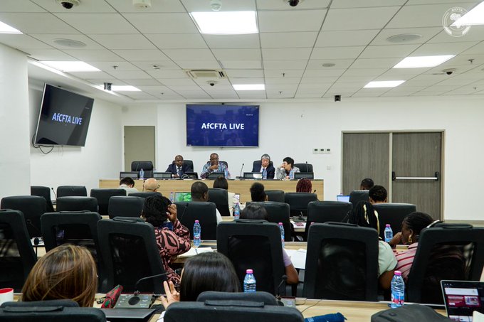 A conference room showing an 'AfCFTA LIVE' panel discussion with several speakers seated at a table facing an audience, with screens displaying the event name.