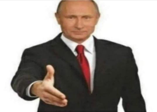 Vladimir Putin in a dark suit with a red tie extends his hand in a handshake gesture against a white background.