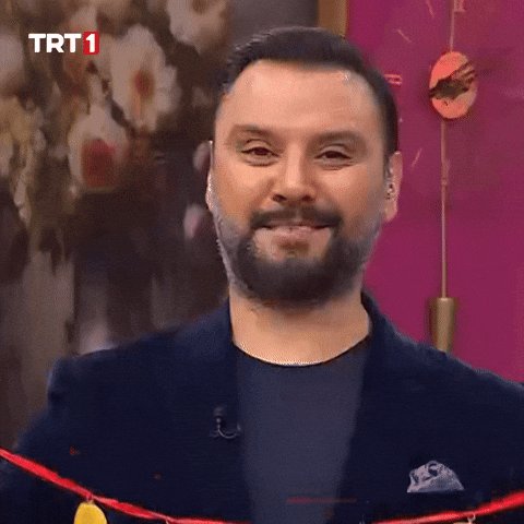 A bearded man in a dark blazer smiles on a TRT 1 broadcast, appearing to comment on gold (XAU) and silver (XAG) prices. The "TRT 1" logo is visible in the upper left corner of the screen.