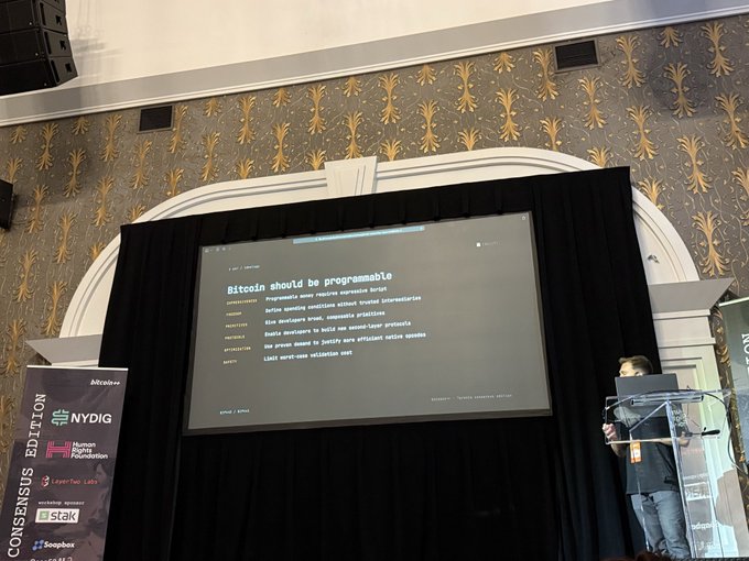 A speaker at a Bitcoin conference presenting a slide titled 'Bitcoin should be programmable,' with sponsor logos for NYDIG, Human Rights Foundation, and others visible on banners.