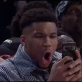 A young man in a checkered shirt with a surprised, open-mouthed expression, appearing to be at a sporting event.