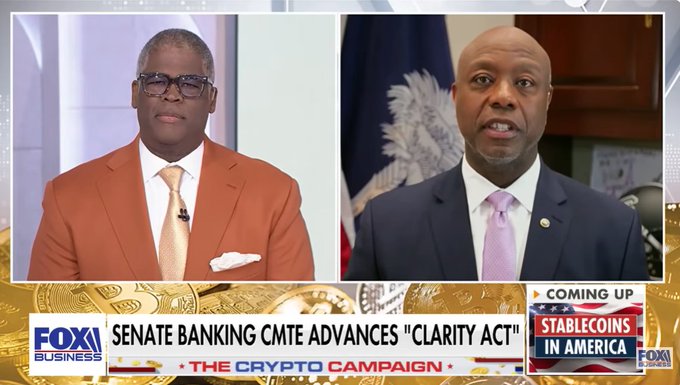 In the image, two men wearing suits are standing next to each other, with one man speaking into a microphone while the other listens attentively. The background features a banner that reads "THE CLARITY ACT IS THE FUTURE OF FINANCE! Sen. Tim Scott: " and "focus on what is in the image and how it relates to the post". This suggests that the image might be related to a political event or discussion, possibly about the clarity act and its implications for the crypto industry.