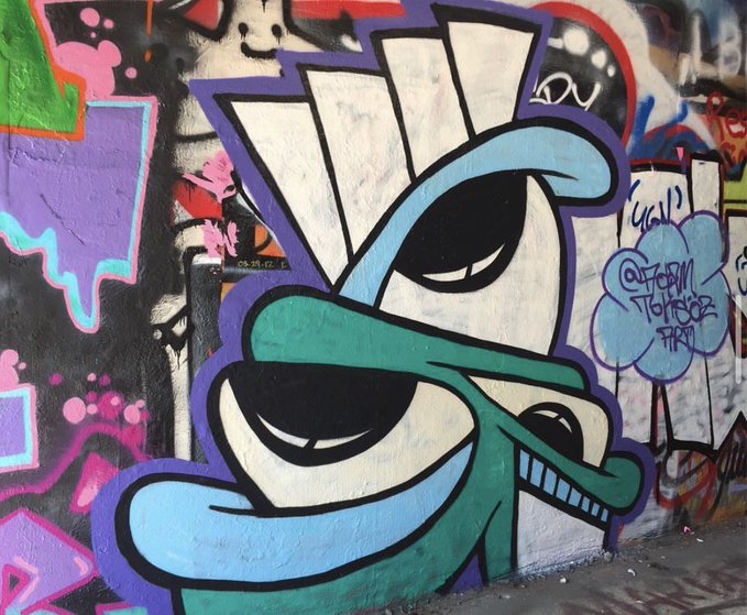A colorful piece of graffiti art on a wall depicting a stylized character with spiky hair and green sunglasses.