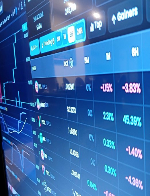 A digital screen shows financial market data with various stock tickers including NOCE, GEX, HCH, EXAS, and PRFX, displaying percentages and 24-hour trading volume in blue tones.