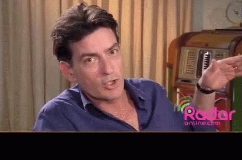 The image features a man wearing a blue shirt, sitting down with his hand raised as if he's about to speak or gesture something out loud. There are two clocks visible in the background, one near the top left corner of the image and another towards the right side. The text "$DOG" is also present in the image.