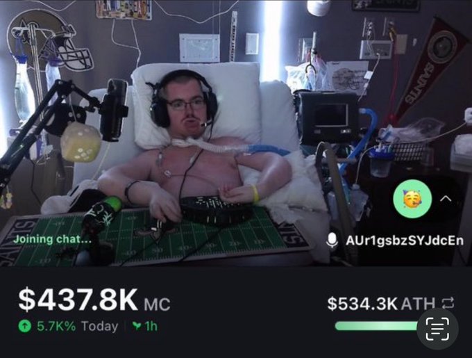 The image shows a shirtless, visibly ill man wearing a breathing apparatus while lying in a hospital bed, appearing to livestream from his room surrounded by medical equipment and memorabilia. A meme coin ticker displays "$437.8K MC" with "5.7% Today," alongside a crypto address "AUr1gsbzSYJdcEn," illustrating the post's claim about someone allegedly running a meme coin scheme from a hospital bed.