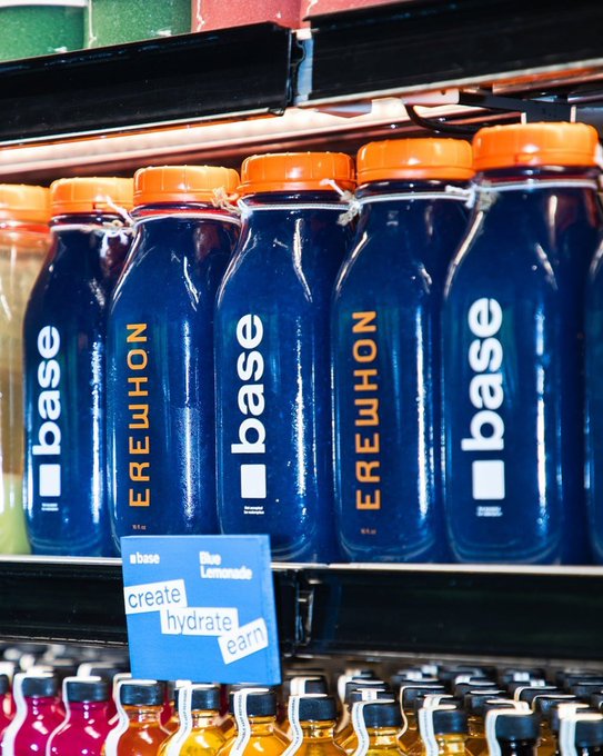 A store shelf displaying rows of blue 'EREWHON' branded water bottles next to a 'create hydrate earn' sign, with other colored beverages visible on the lower shelf.