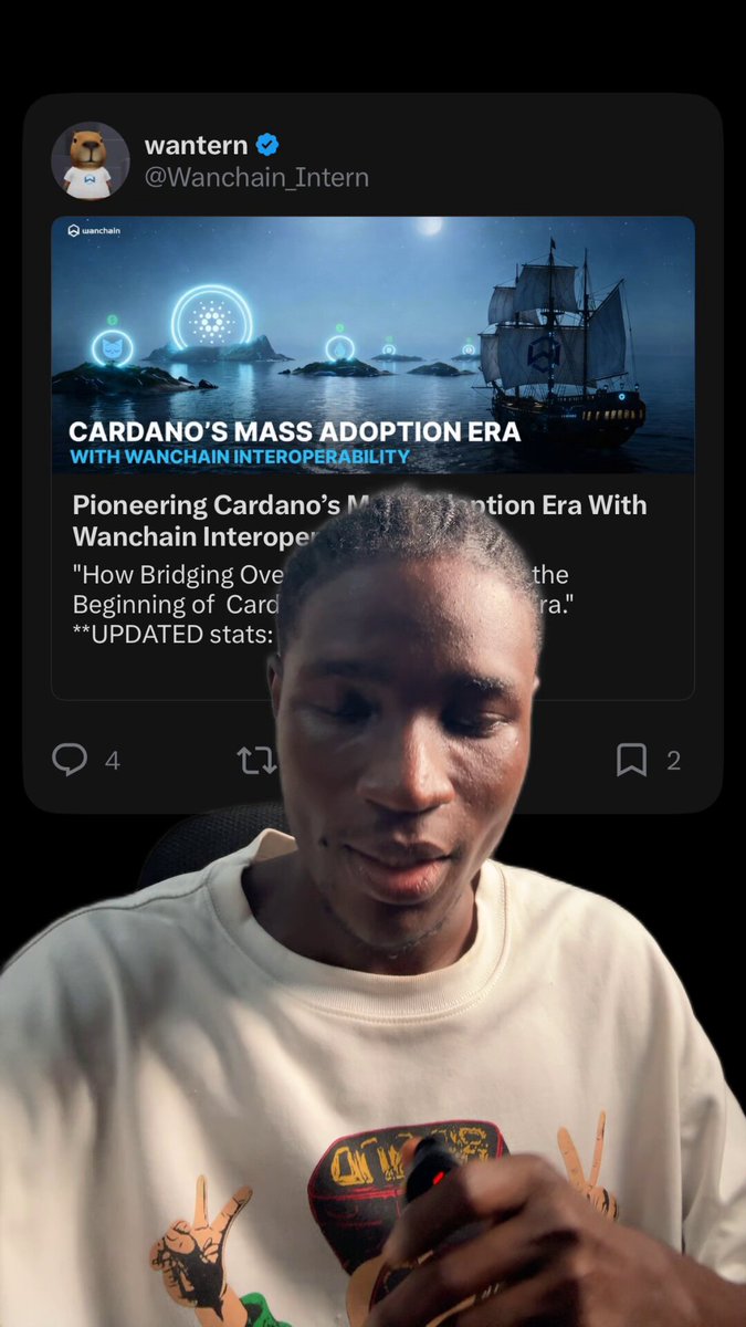 The image shows a man wearing a white shirt holding a cup of coffee, sitting down at his computer desk. The background features a screen displaying a social media post about Cardano's Mass Adoption Era with a picture of a ship on it. The caption reads "Cardano's Mass Adoption Era with WANCHINTERN INTERTM UNITEM" and the image shows a ship sailing in the ocean under a moonlit sky, symbolizing the era when Cardano was introduced to the world as a new cryptocurrency.