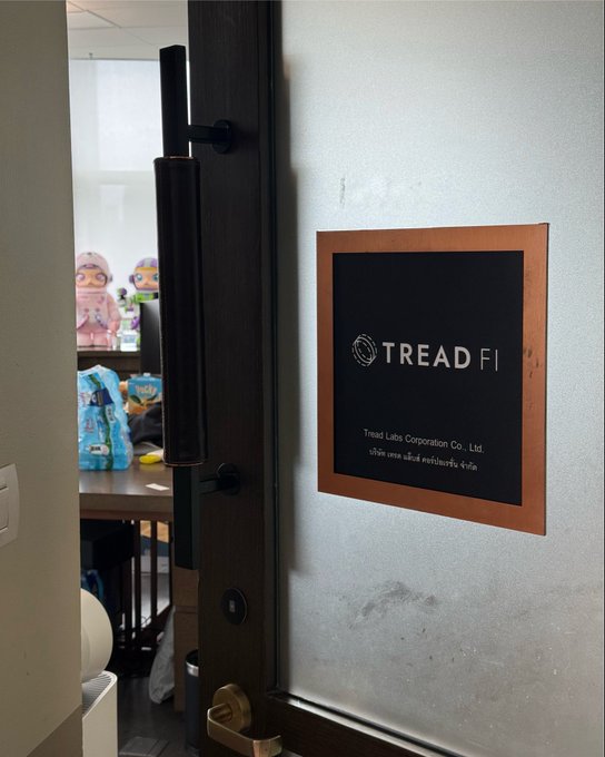 A view through an open door showing a 'TREAD FI' sign for Tread Labs Corporation Co., Ltd., with a glimpse of an office desk containing plush toys in the background.