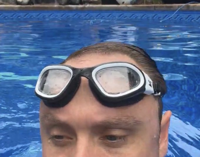 A close-up selfie of a man wearing swim goggles pushed up on his forehead while in a swimming pool.