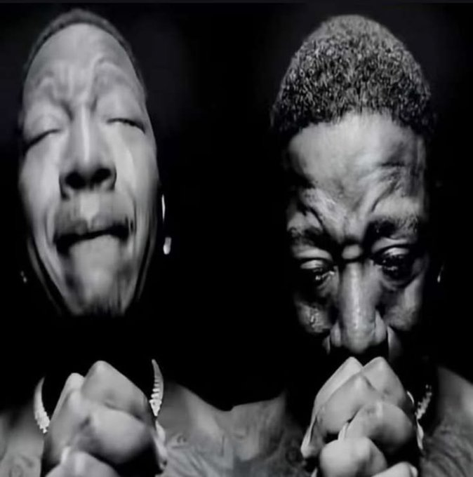 Two men appear in a black-and-white close-up against a dark background, one with closed eyes and another holding a finger to his lips, wearing chains.