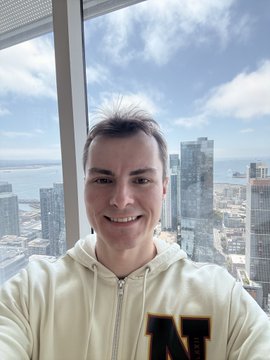 The image features a man wearing a white hoodie with "N" printed on it, smiling at the camera while posing for a photo. The background includes a window overlooking a city skyline, which adds an urban touch to the scene. The caption of the image reads "Great meeting Kevin Leffew from @coinbase ( @kleffew94 )", indicating that the man in the hoodie is possibly discussing or collaborating with someone related to cryptocurrency and payments.