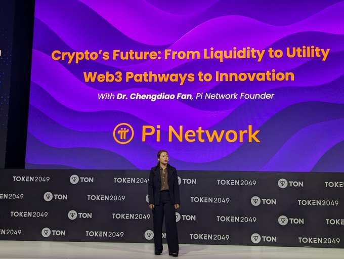 A woman in a dark suit stands on stage at the TOKEN2049 conference, with a large purple backdrop reading "Crypto's Future: From Liquidity to Utility - Web3 Pathways to Innovation" featuring Dr. Chengdiao Fan, Pi Network Founder. The image visually supports the post's discussion about Pi Network's ecosystem growth and utility development seven years after launch.