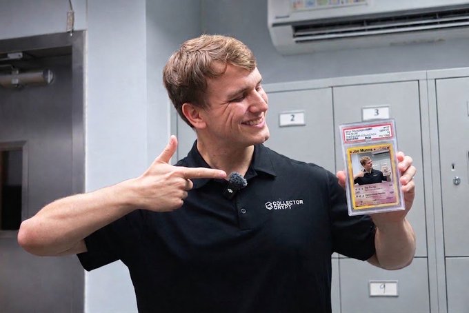 A smiling man wearing a black "COLLECTOR CRYPTO" polo shirt points at a Pokémon trading card he's holding in a PSA grading sleeve, appearing to be in an indoor facility with numbered lockers.