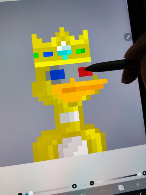 A pixel art drawing of a golden, crown-wearing duck or goose character on a digital tablet screen, with a person's hand holding a stylus actively coloring the character's beak.