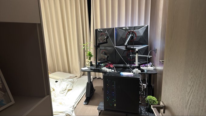A modern home office or gaming setup featuring a dual-monitor desk arrangement, a gaming PC with RGB lighting, and a small daybed.